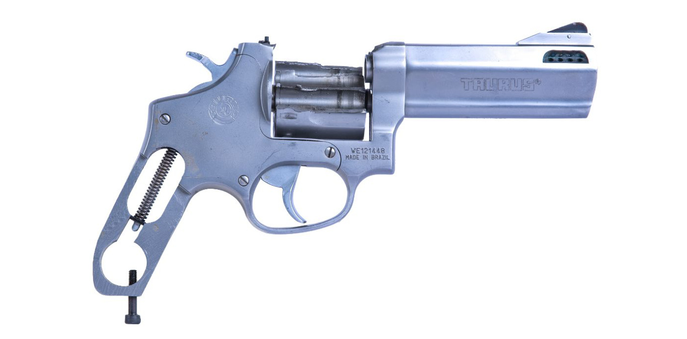 Poškozený nerezový revolver Taurus z boku, bez pažbiček, s odkrytou pružinou v rukojeti